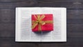Open Bible. Book. Gift in a red package with a gold bow. On a wooden table.