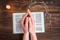Open bible, candle, christian cross and human hands on wooden background. Prayer to God
