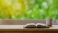 Open Bible and coffee in the morning on a wood table with green nature backgound