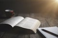 Open bible with a cup of coffee for morning devotion on wooden table with window light. Holy Bible on the small aged wooden table