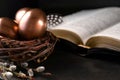 Open Bible on a dark table, eggs in a nest  and feather on dark background. Easter greeting card Royalty Free Stock Photo