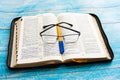 On the open bible lies a pen with glasses, a blue background