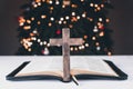 An open Bible on the table. Prayer. Wooden cross. Crucifix. On the background of the Christmas tree. Light and garlands Royalty Free Stock Photo
