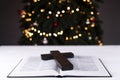 An open Bible on the table. Prayer. Wooden cross. Crucifix. Holy. On the background of the Christmas tree. Light and garlands Royalty Free Stock Photo