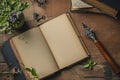 An open blank book lying on a rustic wooden table with a vintage pen, plant, and old books