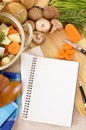 Open blank cookbook or notepad with casserole pot and organic vegetables on kitchen worktop, copy space, vertical Royalty Free Stock Photo