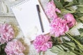 Open blank notepad, pen, and peony on the white wooden table. romantic flat lay.