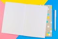 Open blank paper notebook with pen on blue, yellow and pink background. Royalty Free Stock Photo