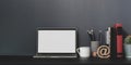 Open blank screen laptop computer in modern workspace with decorations and office supplies on black desk and grey wall Royalty Free Stock Photo