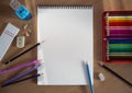 An open, blank sketchbook sheet is positioned vertically. A set of colored pencils, pencils separately, a sharpener and rubber Royalty Free Stock Photo