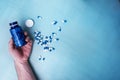 open blue bottle with vitamin pills in the hands of a young man on a blue background