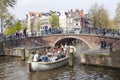 Open boat full of young people under bridge in amsterdam canal o Royalty Free Stock Photo