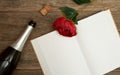 An open book with blank pages, a red rose with green leaves, an open bottle of sparkling wine on a wooden background. Text space. Royalty Free Stock Photo