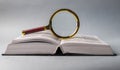 Open book closeup with turning pages and magnifying loupe. Textbook in hard cover on table. Studying and research Royalty Free Stock Photo