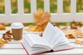 Open book and coffee cup on bench in autumn park