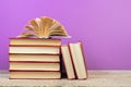 open book. Composition with hardback books, fanned pages on wooden deck table and purple background. Books stacking. Back to Royalty Free Stock Photo