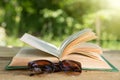 Open book and eyeglasses on a wooden table in a garden. Sunny summer day, reading in a vacation concept Royalty Free Stock Photo