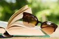 Open book and eyeglasses on a wooden table in a garden. Sunny summer day, reading in a vacation concept Royalty Free Stock Photo