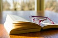 Open book and glasses on a wooden table with sunlight Royalty Free Stock Photo