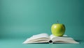 Open book green apple educational concept. Green apple rests on open book, teal background. Knowledge, learning, education, Royalty Free Stock Photo