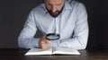 Open book Holy Bible. A man in a shirt sits at a table holding a magnifying glass looks into a book. In the dark. Businessman. Royalty Free Stock Photo