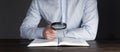 Open book Holy Bible. A man in a shirt sits at a table holding a magnifying glass looks into a book. In the dark. Businessman. Royalty Free Stock Photo