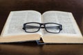 The open book lies on dark wooden table, glasses are on the book