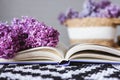 An open book with a lilac branch on a table with a wicker basket