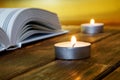 An open book of religious content lies on wooden boards against a golden background. Nearby are lit candles
