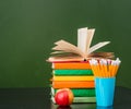 Open book on stack of books near empty green chalkboard Royalty Free Stock Photo