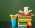 Open book on stack of books near empty green chalkboard Royalty Free Stock Photo