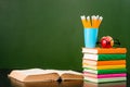 Open book with stack of books near empty green chalkboard Royalty Free Stock Photo