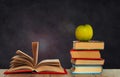 Open book textbook, pile of books and green apple on a wooden desk on the background of a green school chalkboard. Back to school Royalty Free Stock Photo