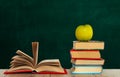 Open book textbook, pile of books and green apple on a wooden desk on the background of a green school chalkboard. Back to school Royalty Free Stock Photo