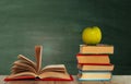 Open book textbook, pile of books and green apple on a wooden desk on the background of a green school chalkboard. Back to school Royalty Free Stock Photo