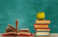 Open book textbook, pile of books and green apple on a wooden desk on the background of a green school chalkboard. Back to school Royalty Free Stock Photo