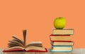 Open book textbook, pile of books and green apple on a wooden desk on the pink orange background. Back to school distance home Royalty Free Stock Photo