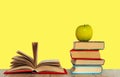 Open book textbook, pile of books and green apple on a wooden desk on the yellow background. Back to school distance home Royalty Free Stock Photo