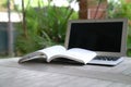 Open book on top of computer laptop. Garden view. Home setting