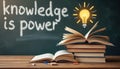 Open books stack on wooden table near chalkboard with text knowledge is power and drawing of lightbulb. Education, learning, idea Royalty Free Stock Photo