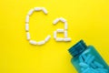 Open bottle and calcium symbol made of white pills on yellow background, flat lay Royalty Free Stock Photo