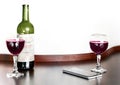 Open bottle and two glasses of red grape wine and mobile phone on brown wooden table and white blurred wall background. Alcohol dr Royalty Free Stock Photo