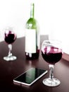 Open bottle and two glasses of red wine and a mobile phone on brown wodden table and white blurred wall background. Alcohol drink Royalty Free Stock Photo