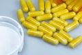 An open bottle of yellow capsules laying across a white table Royalty Free Stock Photo