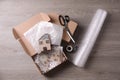 Open box with decorative house figures, adhesive tape, scissors, foam peanuts and bubble wrap on wooden table, flat lay Royalty Free Stock Photo