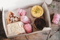 open box with different cakes and marshmallows, on a wooden background. Assorted pastries in a box