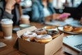 an open box of doughnuts on a table with two women Royalty Free Stock Photo