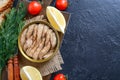 Open can of spicy smoked sprats in oil on a black background with lemon, bread, fresh tomatoes. Royalty Free Stock Photo
