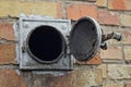 Open circular heating hood with black soot and gray iron cover on the brown brick wall