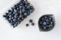 Open clamshell container of blueberries on a white granite counter, small black bowl